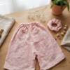 Ensemble composé d'un short ample à taille élastique et d'un chouchou assorti en double gaze de coton de couleur vieux rose, posés sur une table en bois.