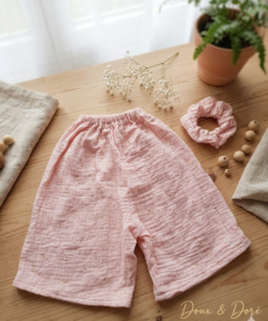 Ensemble composé d'un short ample à taille élastique et d'un chouchou assorti en double gaze de coton de couleur vieux rose, posés sur une table en bois.