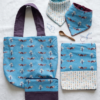 Coffret cadeau bébé artisanal : accessoires textiles assortis en coton bleu avec motifs ratons laveurs et formes géométriques.