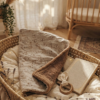 Une couverture pour bébé en coton crème imprimé d'oursons rétro, repliée dans un couffin en osier pour montrer sa doublure en sherpa marron moelleuse.