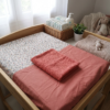 Housse de matelas à langer bicolore à motif floral et tissu terracotta, surmontée de sa serviette en éponge assortie sur une table à langer en bois.